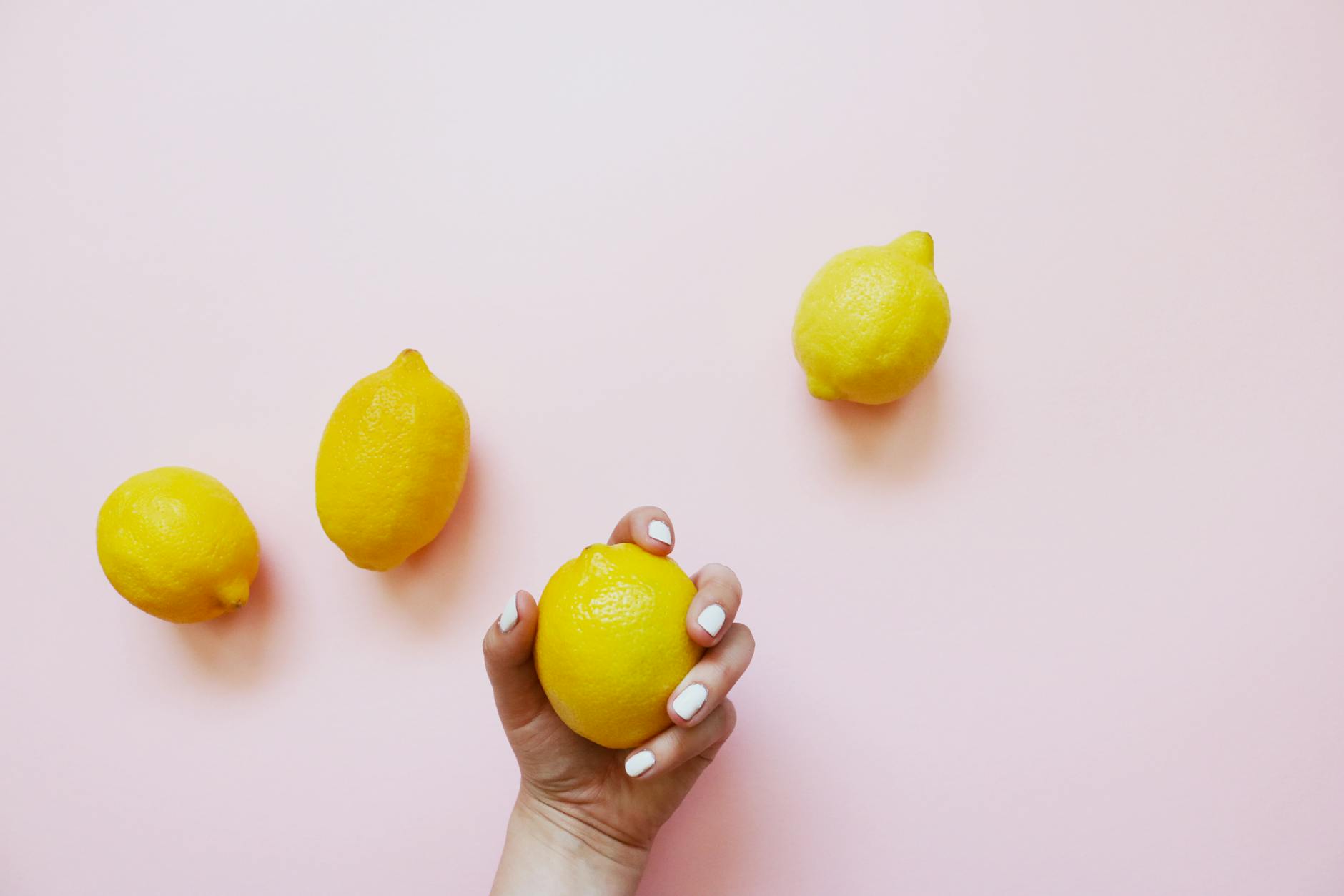 A hand holding a bright lemon against a soft pink background with additional lemons nearby, symbolizing fresh exploration and discovery