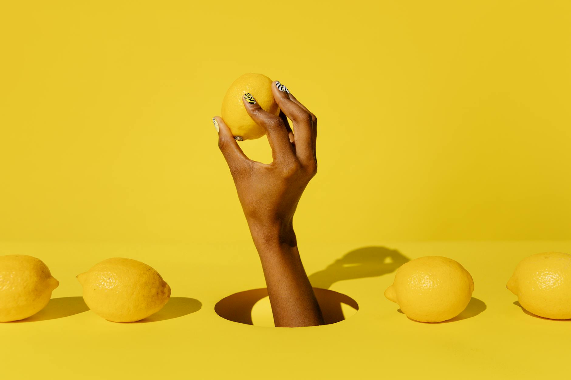 Hand holding a fresh lemon against a bright yellow background, symbolizing pleasure without pressure