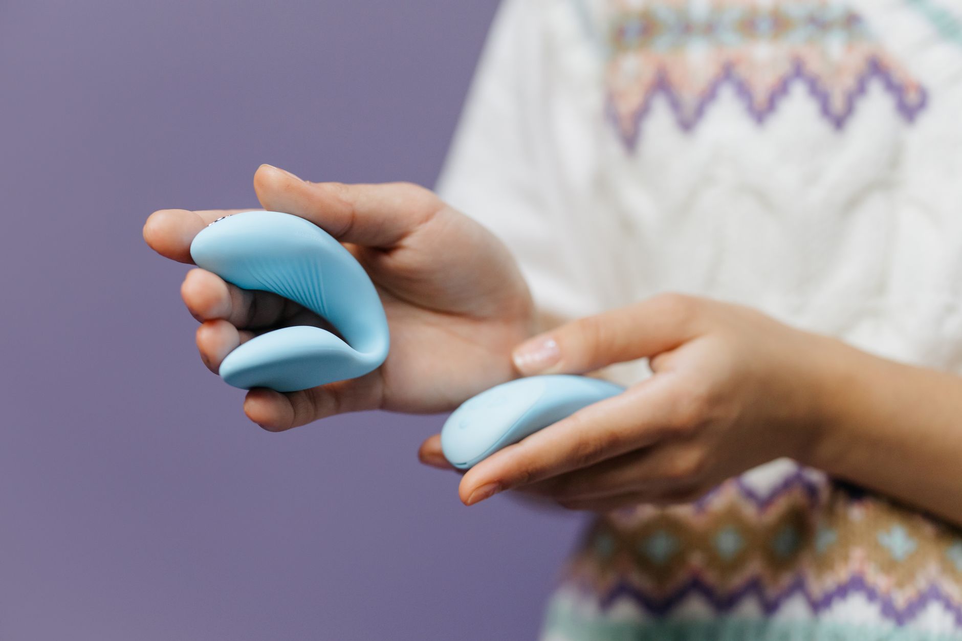 Close-up of hands holding a sleek blue vibrator against a purple background, representing spontaneous pleasure and intimate moments.