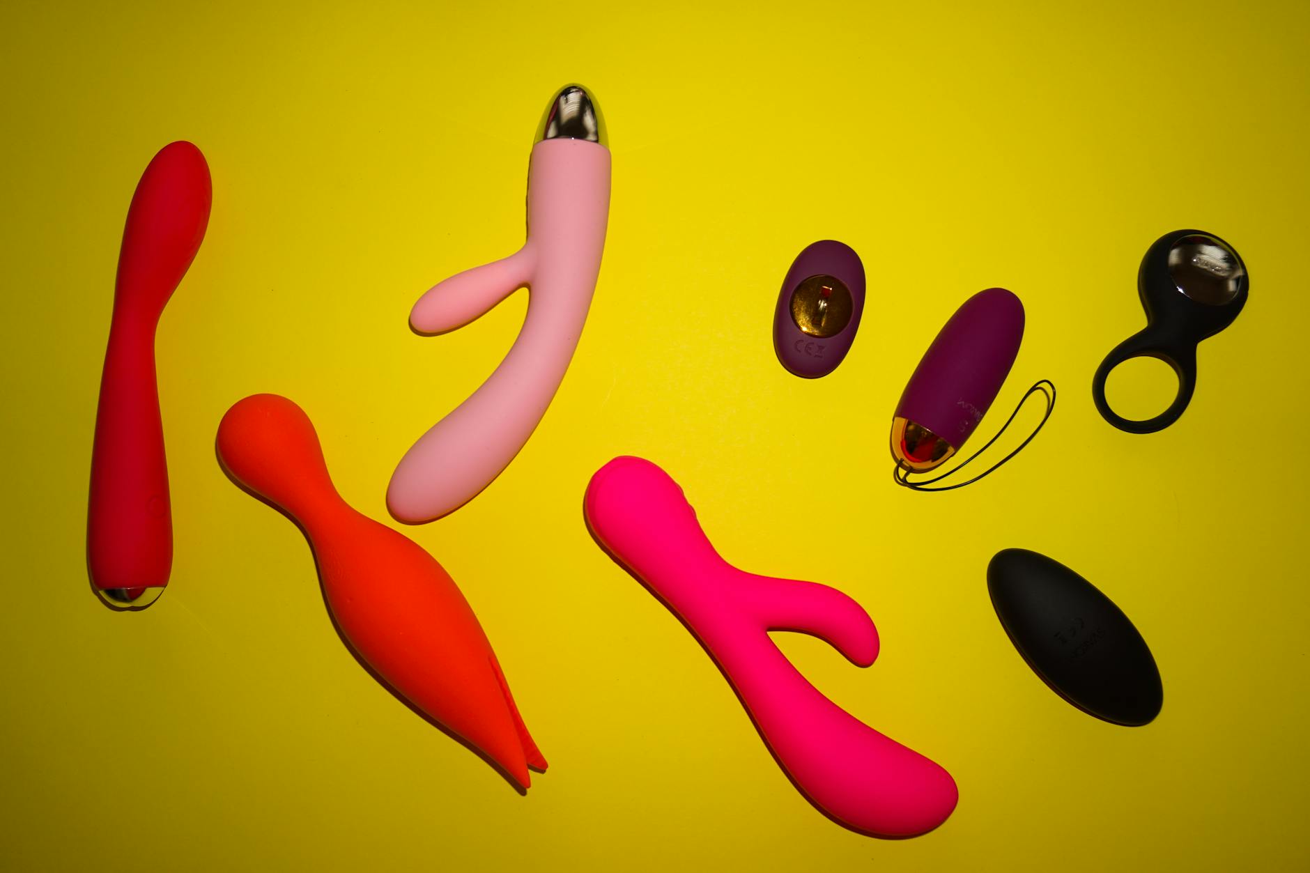 Collection of colorful vibrators arranged on a bright yellow surface showing design diversity and modern adult wellness options